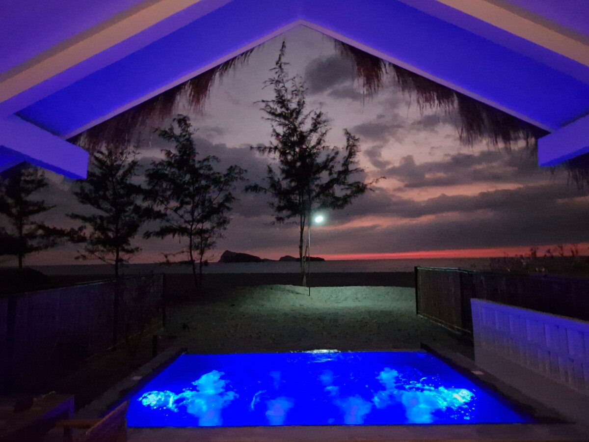 Blue-lit pool at night with sunset sky and island silhouette